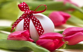 Яйцо с бантом на столе с тюльпанами на праздник Пасха