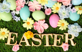 The inscription on the grass with colorful eggs and flowers for Easter