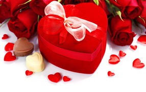 Red box in the shape of a heart on a table with roses and sweets for a loved one