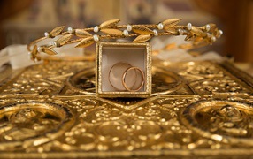 Two gold wedding rings in a box with a wreath