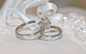 Two wedding rings on a pillow with a ribbon