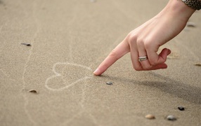 Девушка рисует сердце на песке 