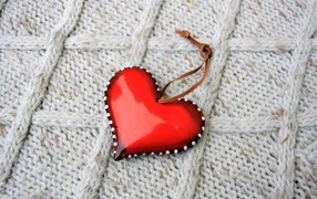 Красное сердце лежит на вязаном свитере 