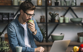 Мужчина с ноутбуком ест яблоко в кафе 