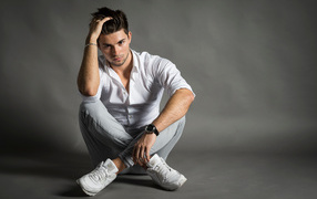 Красивый молодой человек в белой рубашке сидит у стены 