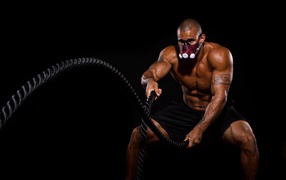 Накаченный мужчина в маске с канатом в руках 