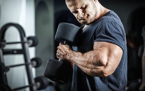 Мужчина бодибилдер в спортзале с гантелей 