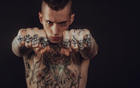 Мужчина с татуировками на теле с перстнями на пальцах