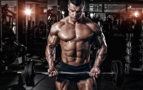 Мускулистый мужчина со штангой в руках в спортзале