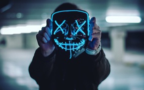 Неоновая маска анонима в руках у парня 