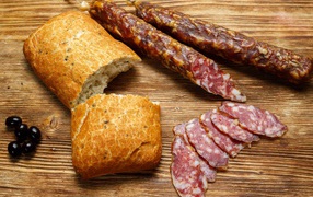 Сухая колбаса на столе с батоном и оливками