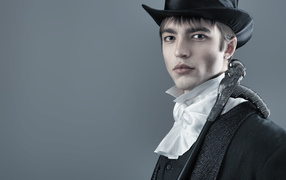 Красивый молодой человек в черном цилиндре и фраке на сером фоне