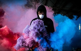 Мужчина в маске с разноцветными дымовыми шашками