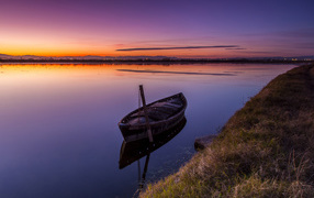 Старая лодка стоит в воде на закате солнца 