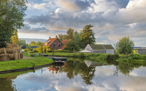 Дома отражаются в реке под небом с белыми облаками