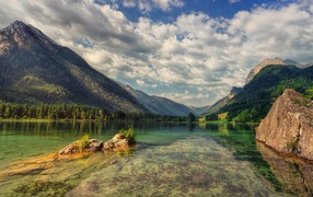 Большие камни в озере на фоне гор под небом с белыми облаками