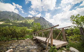 Старый деревянный мост через речку на фоне гор
