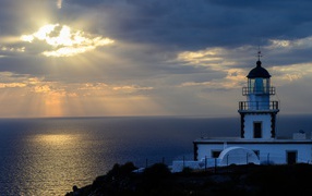 Белый маяк на берегу в лучах солнца у моря 