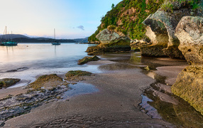 Мокрый песок и большие каменные глыбы на берегу залива