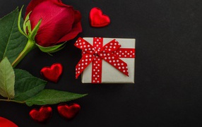 Маленький подарок и красная роза на черном столе