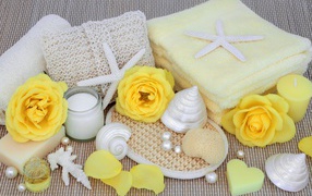 Желтые розы на столе с полотенцем, ракушками и мылом