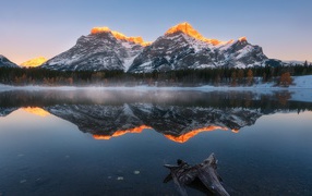 Вершины гор в лучах солнца отражаются в чистой воде озера