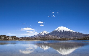 Заснеженные вершины гор под голубым небом отражаются в воде 
