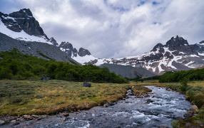 A fast river at the snow-capped mountains under thick white clouds