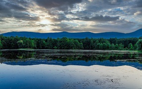 Солнце пробивается сквозь облака в небе над озером
