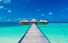Деревянный мост к домам на сваях в голубом океане 