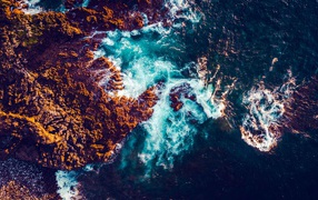 Белые морские волны бьются об камни, вид сверху