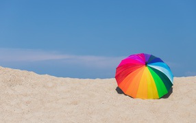 A multi-colored umbrella lies on the hot sand in the summer