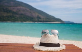 A white hat with glasses lies on a bench by the sea
