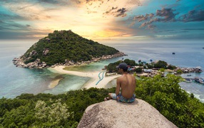 Мужчина сидит на краю скалы на закате 