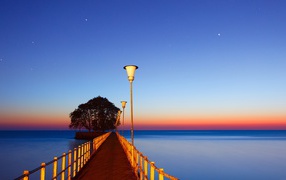 Мост в фонарями в море на закате 