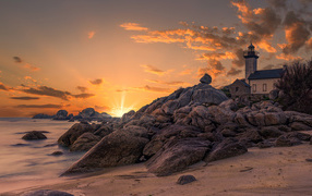 Маяк на берегу каменного берега на закате 