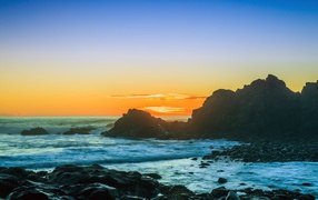 Закат солнца над океаном с камнями на берегу 
