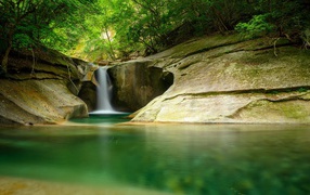Водопад стекает по скале в озеро в лесу
