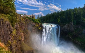 Быстрая вода водопада стекает с утеса у хвойного леса 