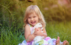 Довольная маленькая девочка обнимает белого кролика на траве 