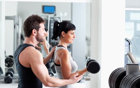 Девушка занимается в спортзале с тренером