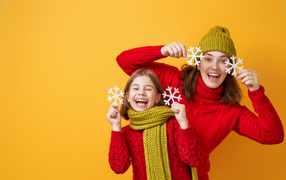 Веселые мама и дочка в красных свитерах на оранжевом фоне