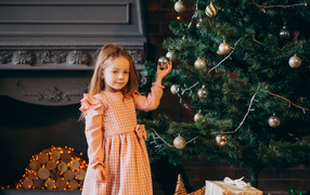 Милая маленькая девочка стоит у наряженной елки 