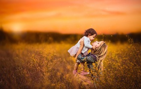 Девушка держит маленькую девочку на руках в поле на закате