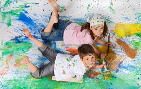 Маленькие мальчик и девочка рисуют красками на полу 