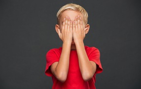 Маленький мальчик в красной футболке закрыл лицо руками 