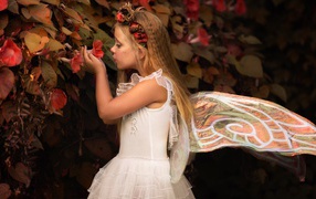 Маленькая девочка в костюме феи стоит у цветов