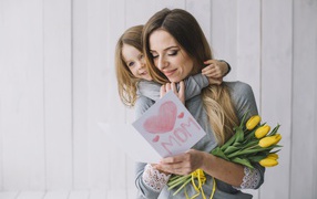 Маленькая девочка подарила маме открытку и букет тюльпанов