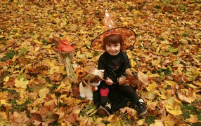 Маленькая девочка в костюме ведьмы сидит на опавшей листве на Хэллоуин