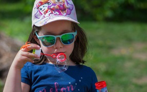 Маленькая девочка в очках с мыльными пузырями